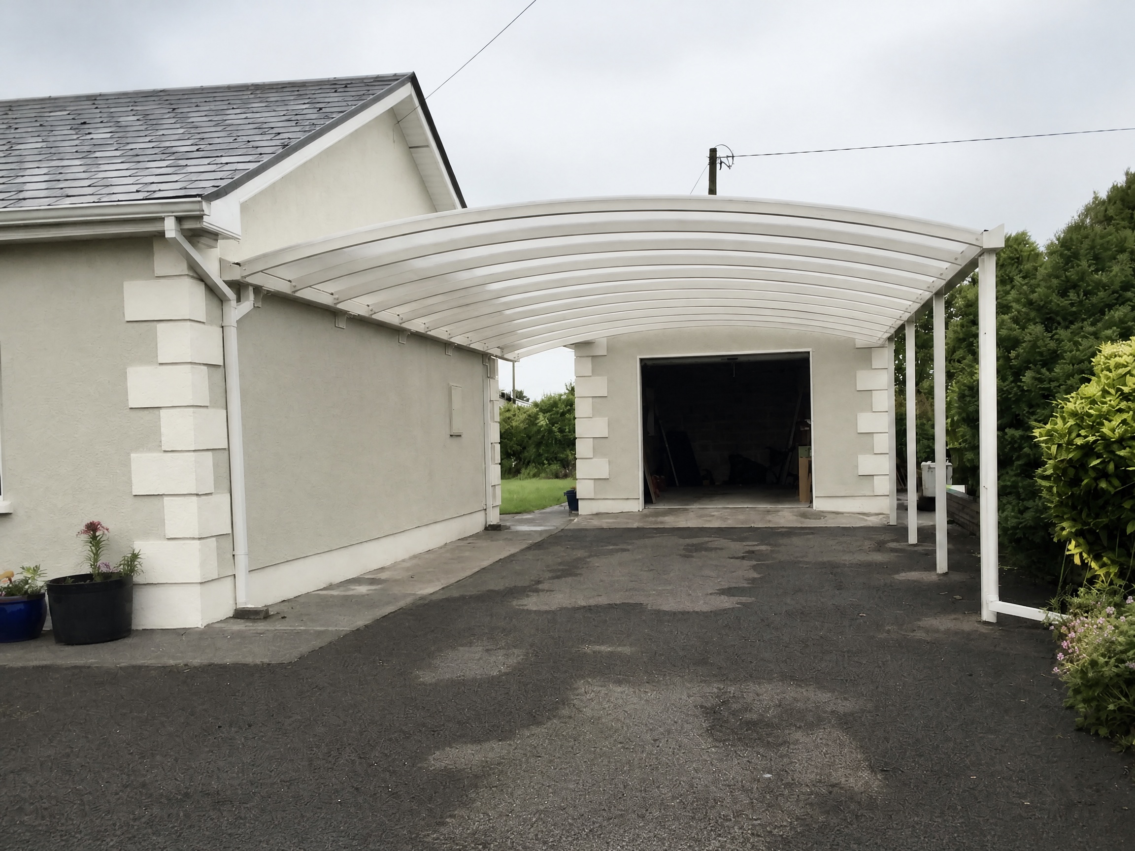 Curved white canopy installed beside a home and garage